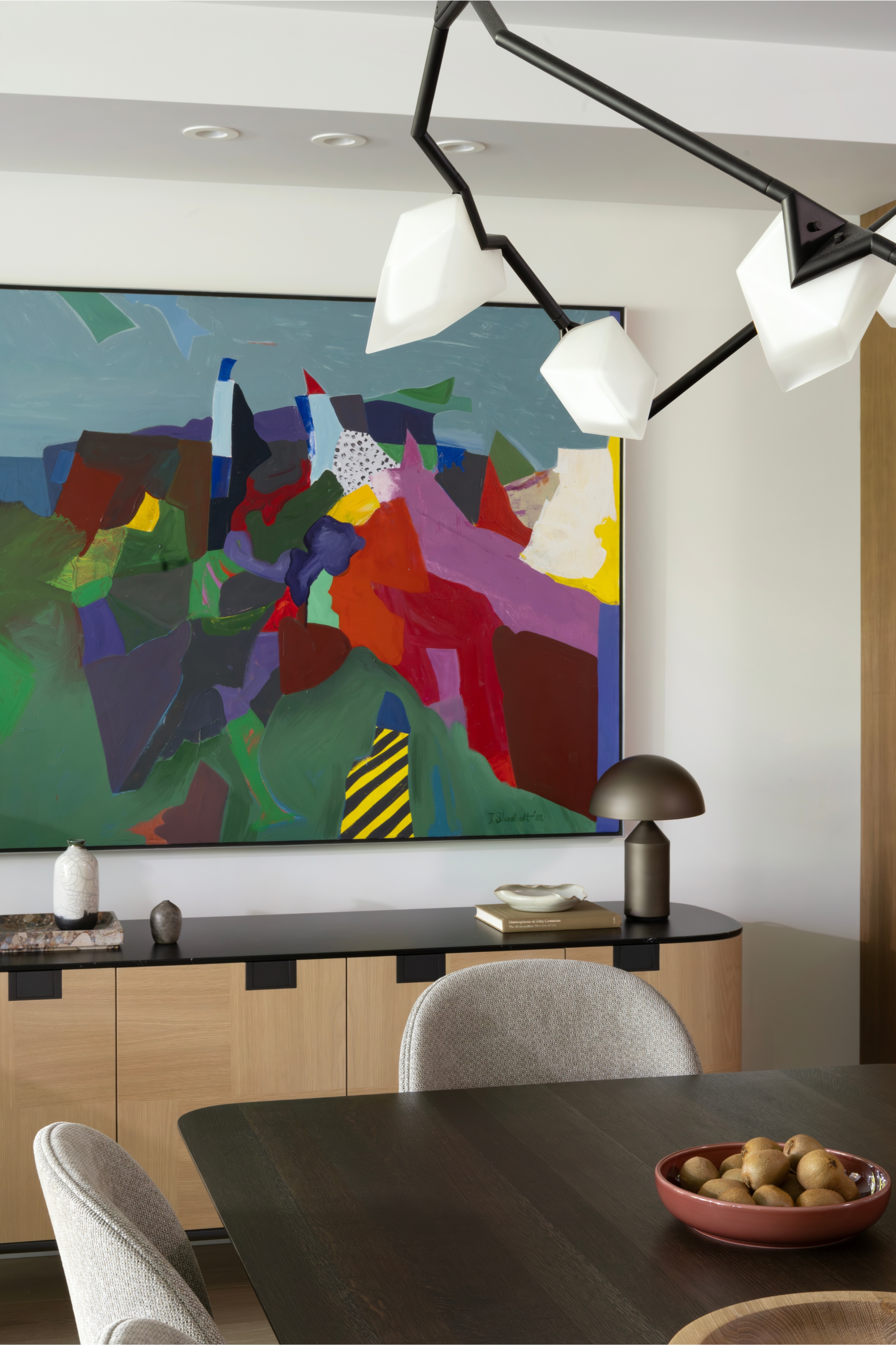 a dining room with a side board with an atollo lamp on with a brightly colored artwork above