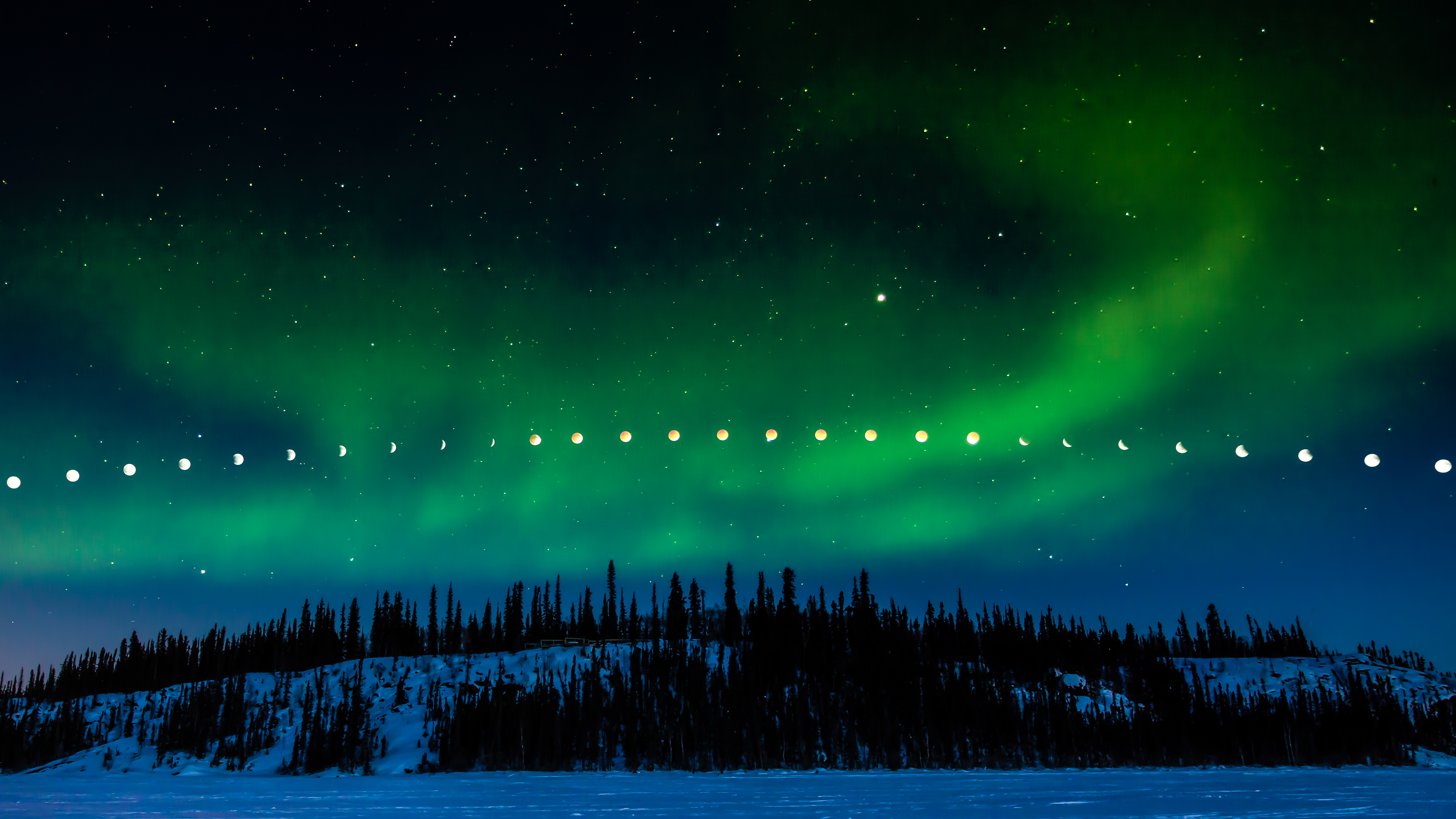 A lunar eclipse takes place above Prelude Lake while the Aurora Borealis puts on a show, in this composite image from Prelude Lake Territorial Park, Northwest Territories, Canada.