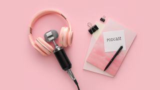 Microphone, headphones, stationery and paper sheet with word PODCAST on pink background