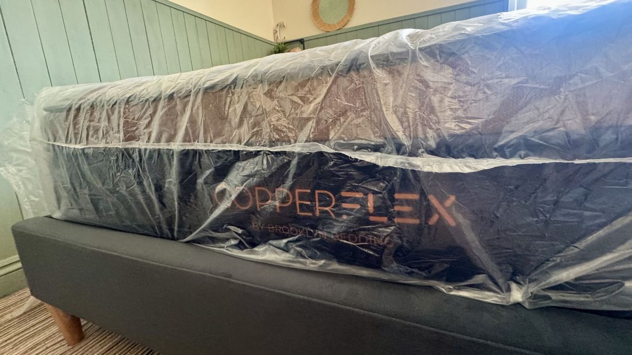 Navy and bronze Brooklyn Bedding Copperflex Memory Foam mattress with plastic wrapping on on grey bed frame