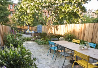 narrow garden ideas New York city garden with concrete slabs and trees and yellow dining chairs
