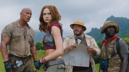 From left to right: Dwayn Johnson looking serious, Karen Gillan looking concerned, Jack Black looking concerned while holding a map, and Kevin Hart looking to the right. 