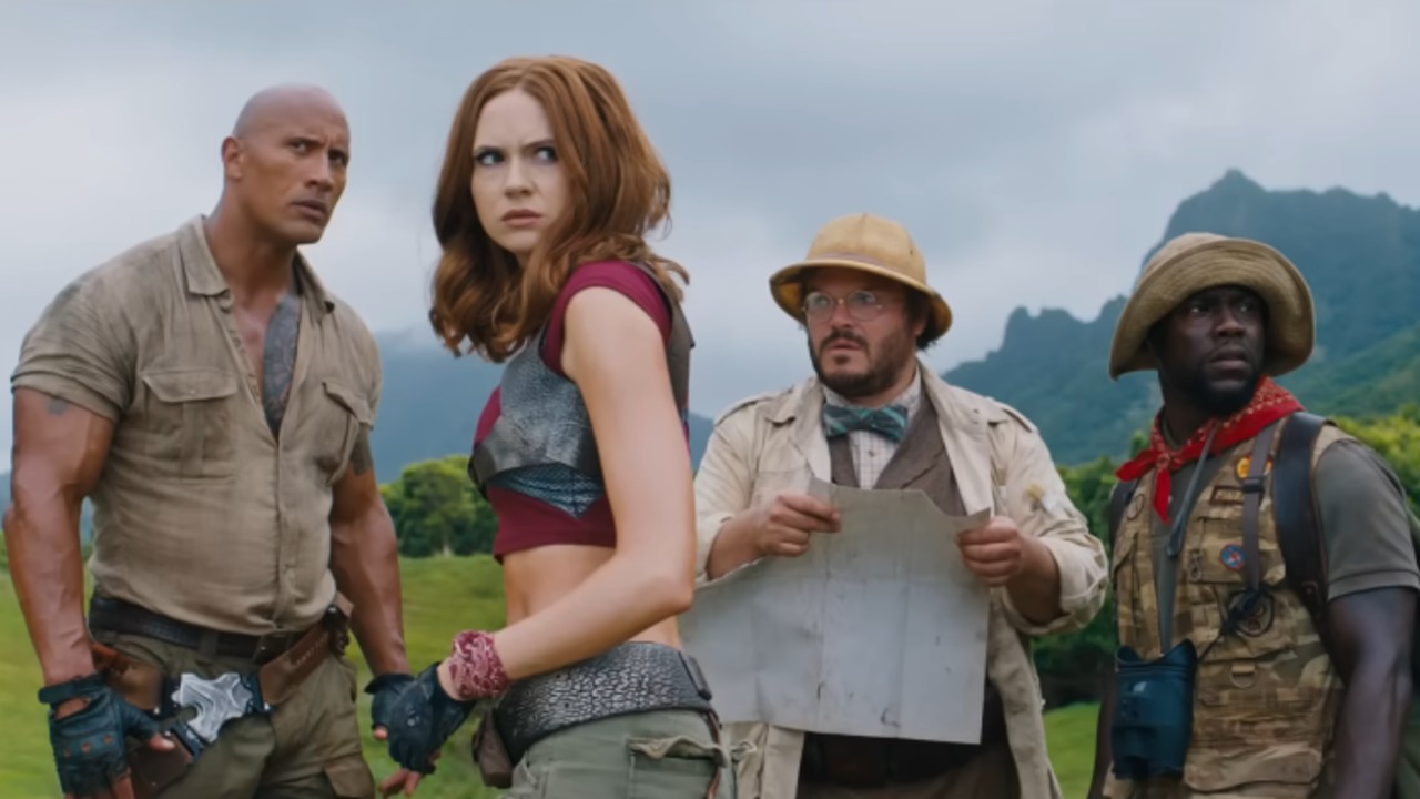 From left to right: Dwayn Johnson looking serious, Karen Gillan looking concerned, Jack Black looking concerned while holding a map, and Kevin Hart looking to the right. 