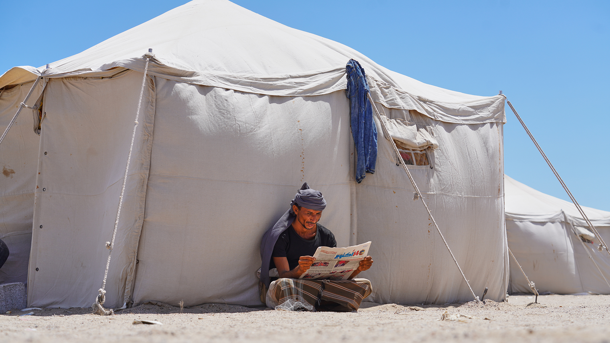 A displaced Yemeni man reads a newspaper at the Al-Firdaws camp in Ras Imran near Aden, Yemen