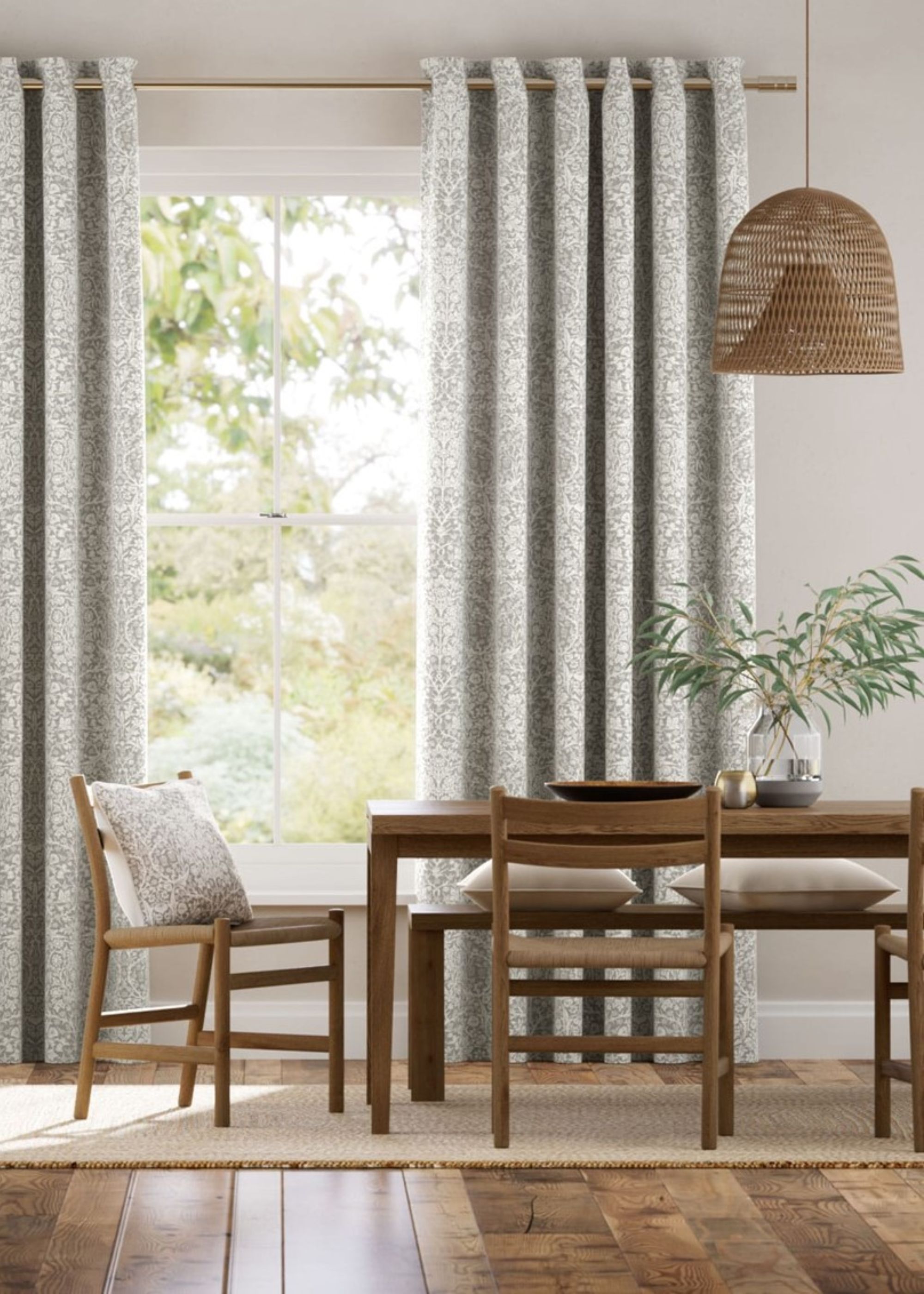 Curtains handing in a dining room with a large dining table in the corner. There is a vase and plant on the table with a pendant light hanging above