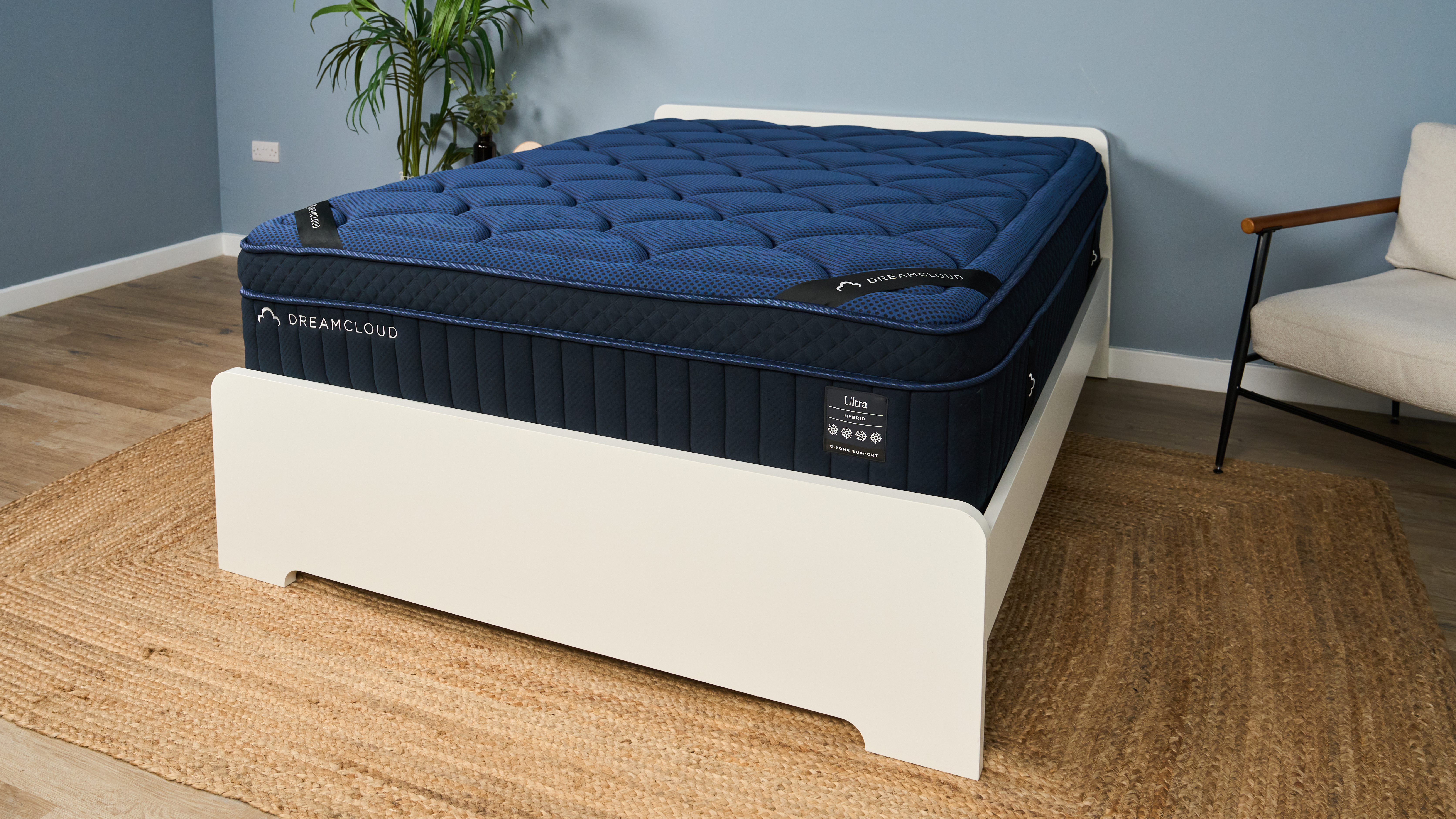 The image shows a navy blue mattress on a white bedframe, which is set in a muted blue bedroom.