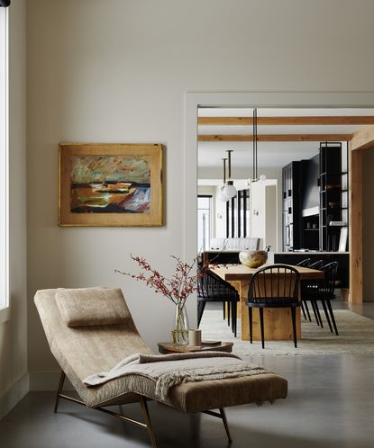 a chaise lounge in the corner of a white living room next to a doorway looking into a dining area