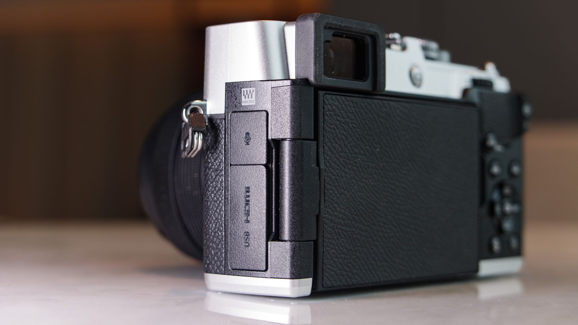 Close up of the OM System PEN mirrorless camera's connection port doors, in a modern room with lantern in the background