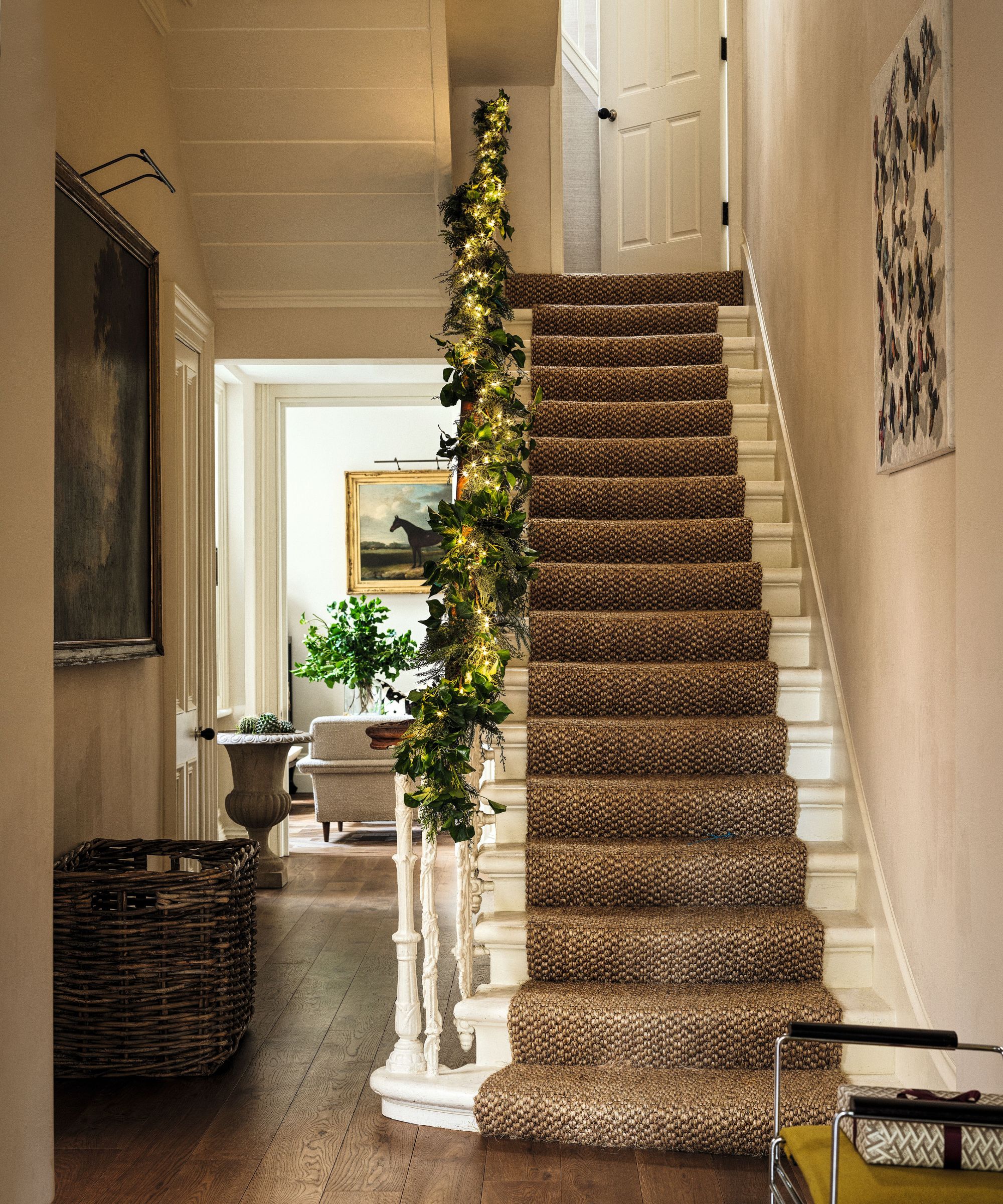 Entryway with cream walls and a garland running up the staircase, the stairs have a brown jute runner