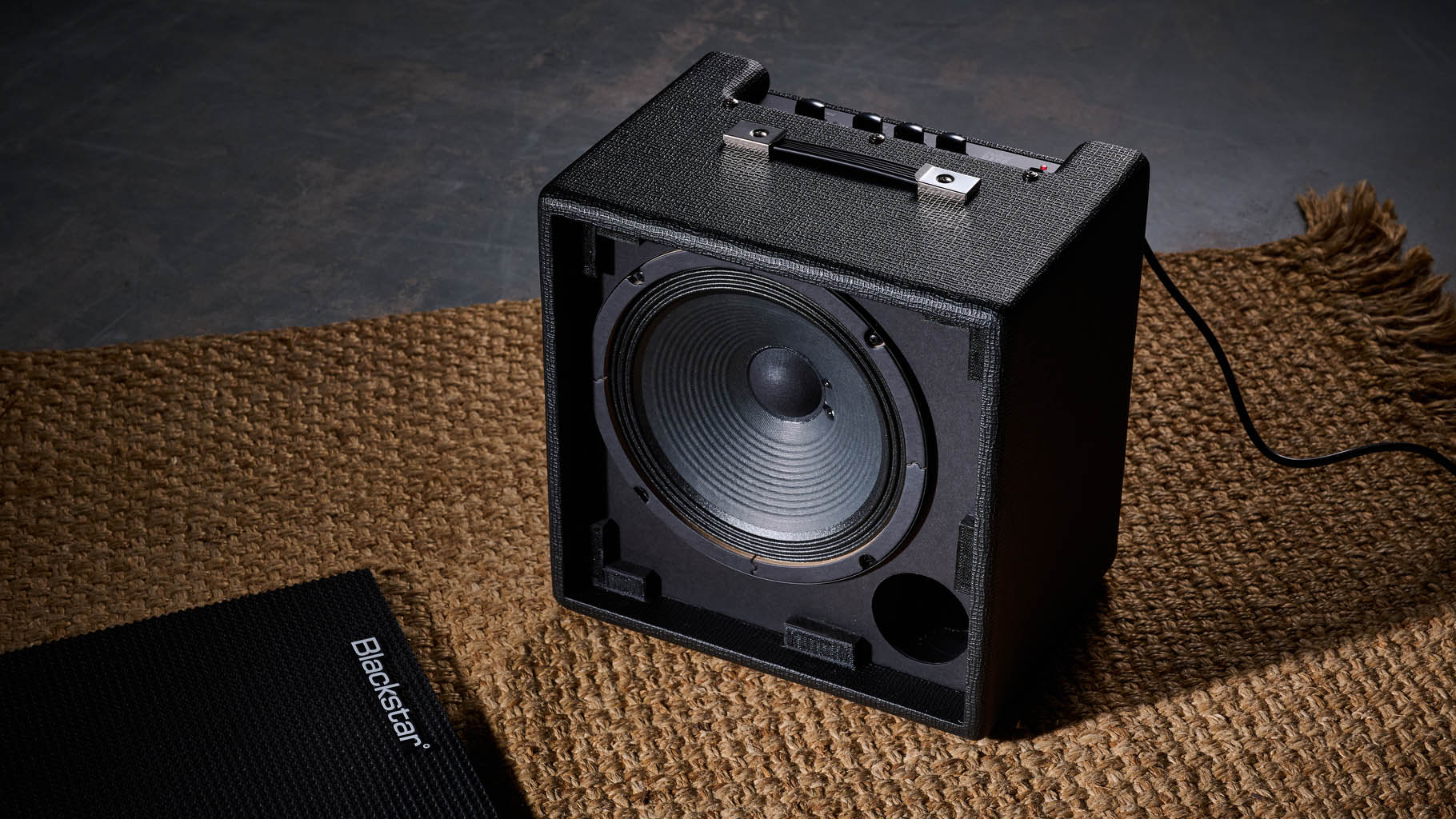 Blackstar Debut Bass 25: this compact little combo is finished in black with matching grille clothe and is photographed in close-up against a stone floor and weaved rug.