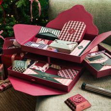 Papier's stationery advent calendar 2025 open on a green armchair next to a Christmas tree decorated with pink and red ribbons