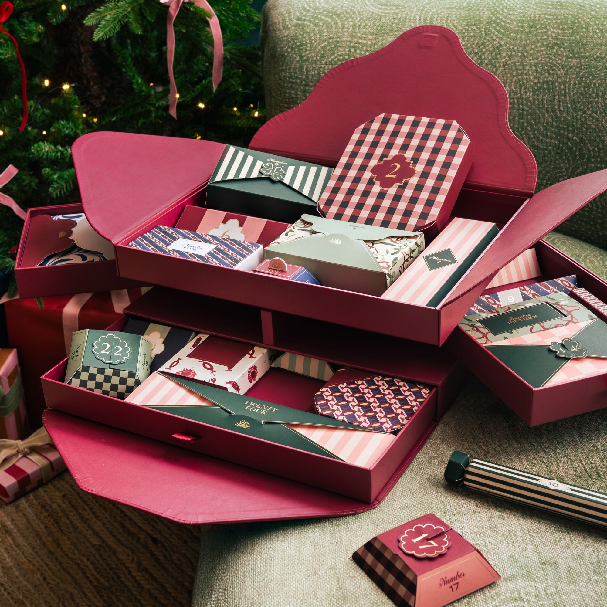 Papier&#039;s stationery advent calendar 2025 open on a green armchair next to a Christmas tree decorated with pink and red ribbons