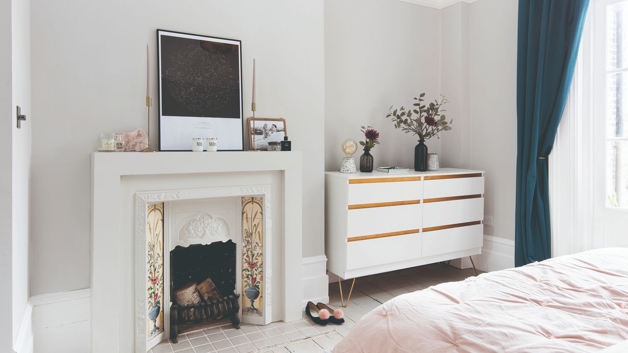 Pale grey wall with TV, behind fireplace and white dressing table. Window with navy blue curtains