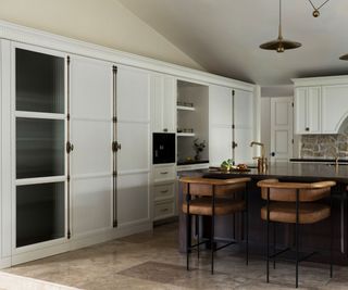 A transitional kitchen with white cabinets with brass, full length locks used as handles