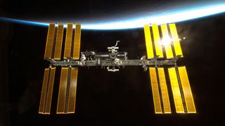 An image of the International Space Station with Earth's atmosphere lit un in the background.