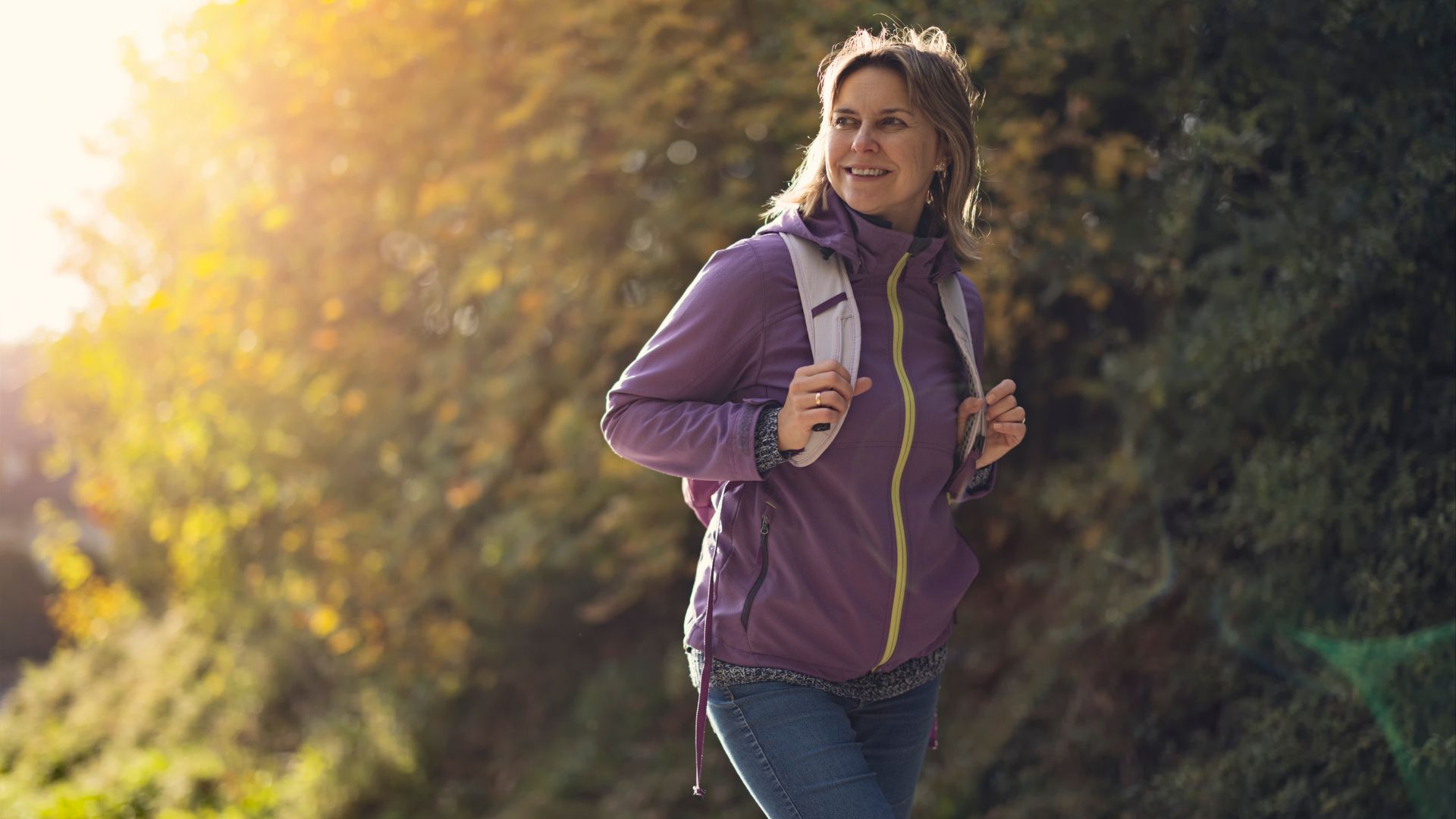 Woman walking in autumn with backpack, smiling
