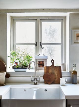 kitchen sink by window with chopping boards and herbs and white walls