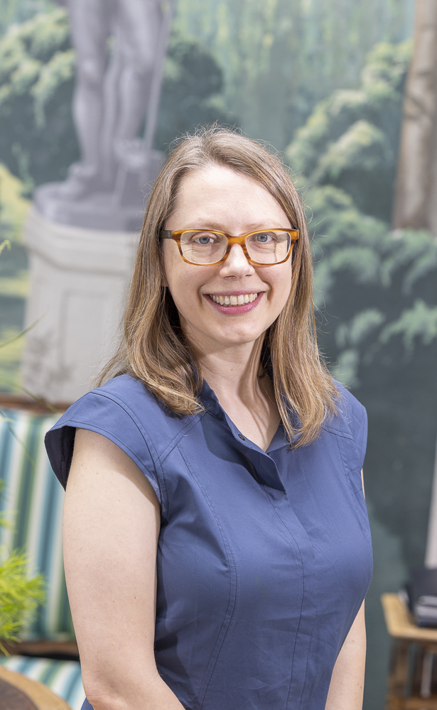 headshot of woman in blue top, with glasses and shoulder length brown hair