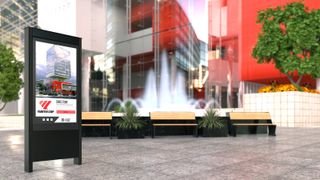 A new Chief LED outdoor kiosk stands in front of a courtyard with a vibrant red building and water fountain.
