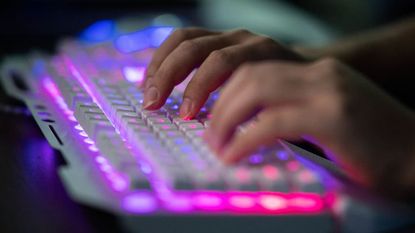 A hacker types on an illuminated keyboard.