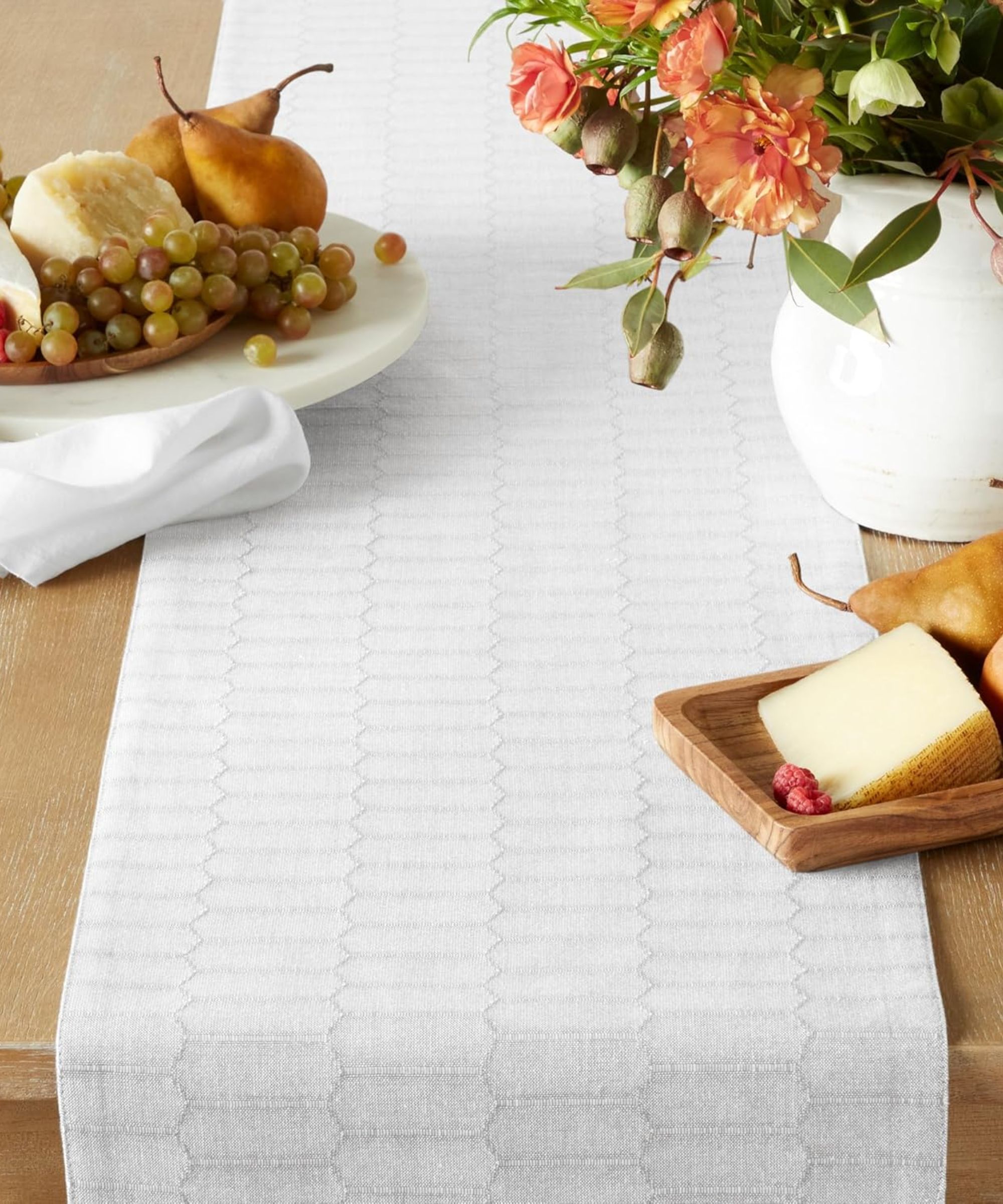 White honeycomb patterned table runner with white vase of flowers and two charcuterie boards