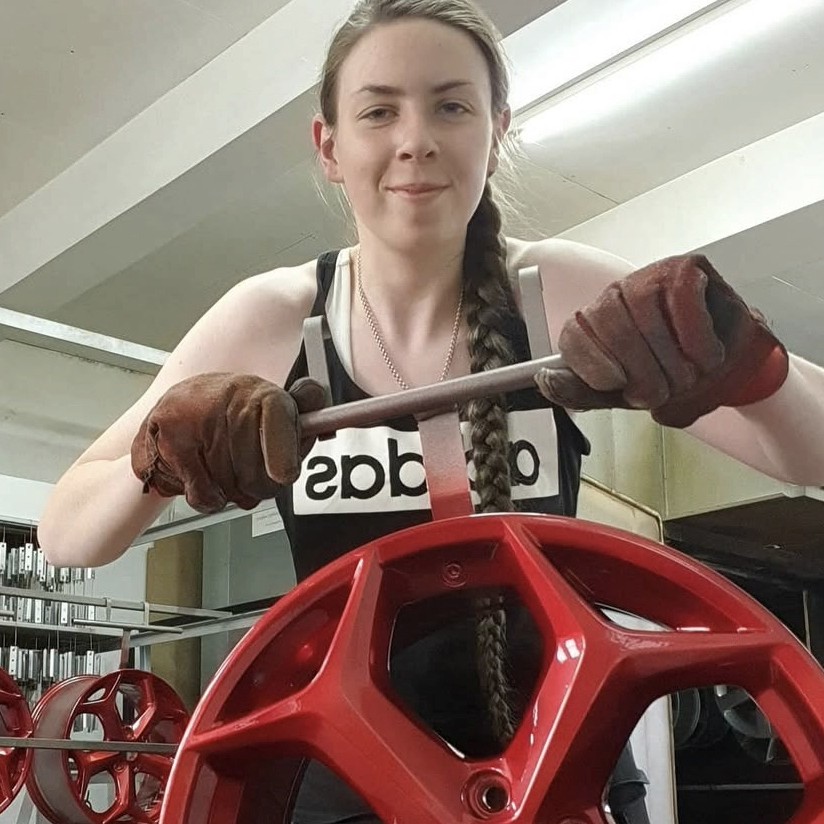 female holding wheel trim in powder coating workshop