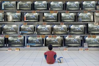 Boy sitting in front of a wall of tvs