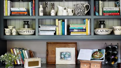 blue painted open shelving in kitchen with books, artwork and crockery