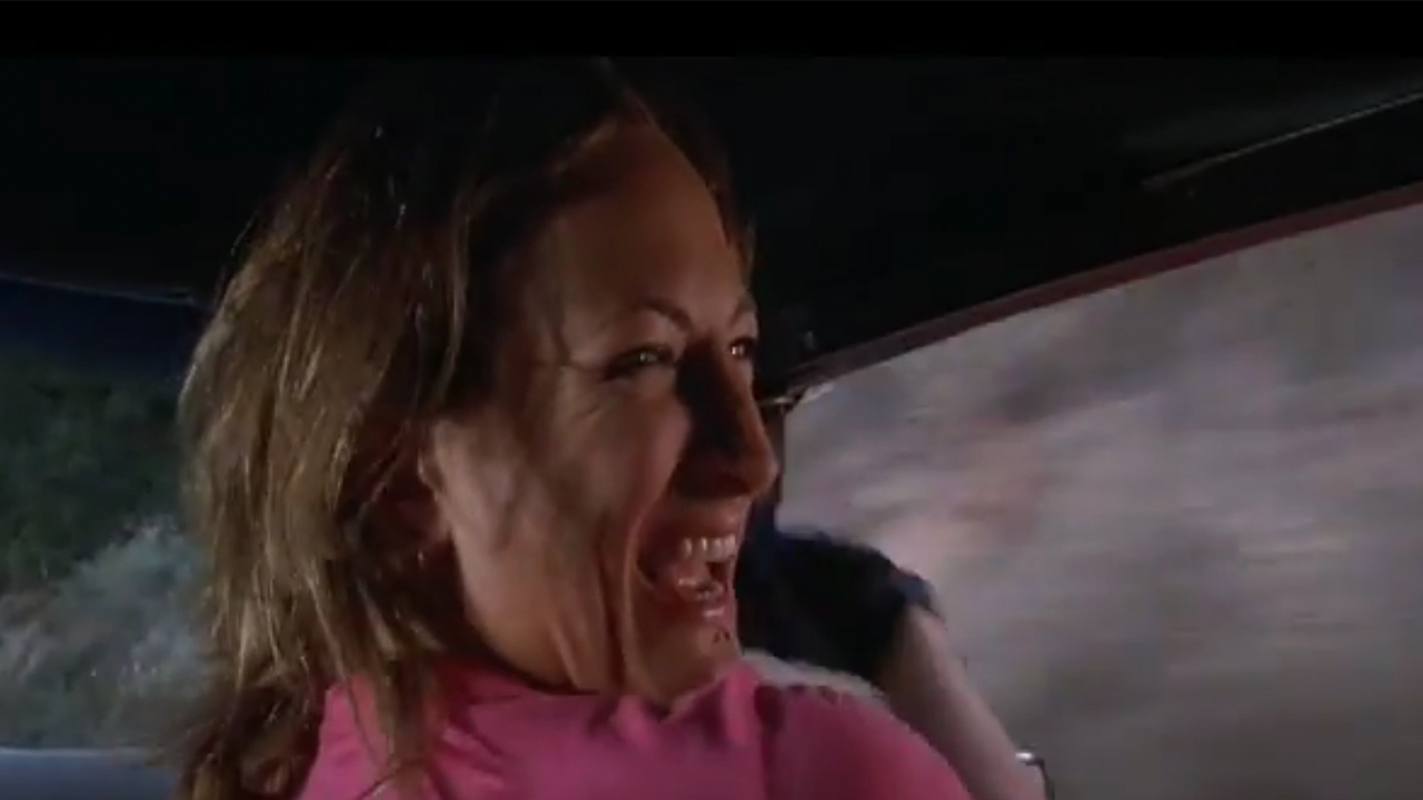 Zoey Bell in a car, looking back over her shoulder and smiling
