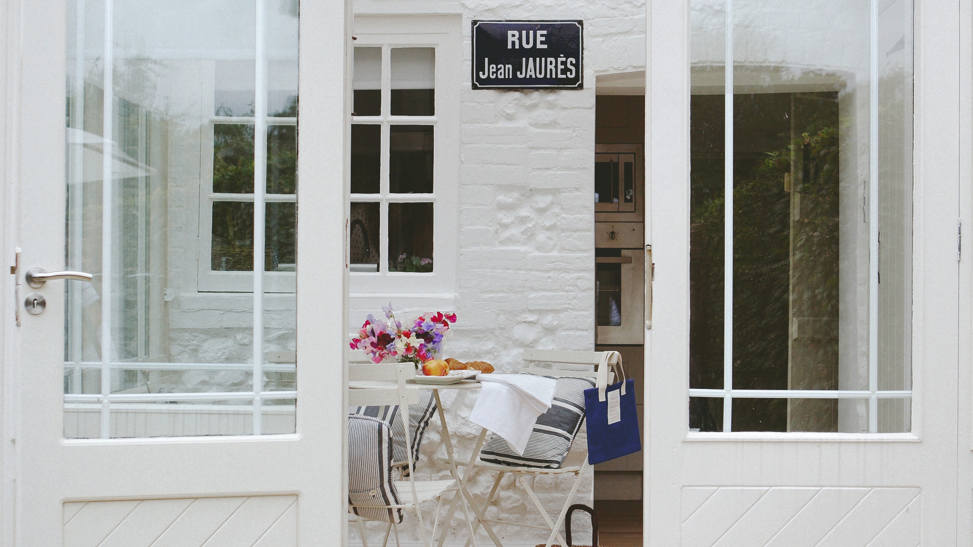 A white conservatory with a white bistro set and striped blue cushions