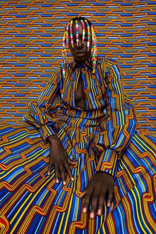 A woman with beads in her hair against a very colorful background