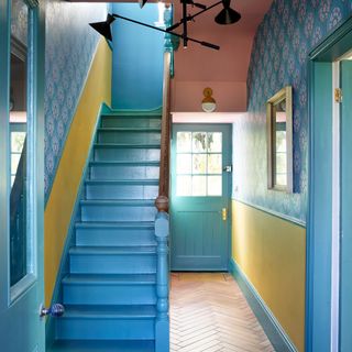 Colourful hallway with stairs painted blue, patterned wallpaper and pink and yellow accents