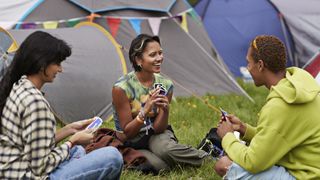 A group of friends sit playing cards in front of tents at a festival.