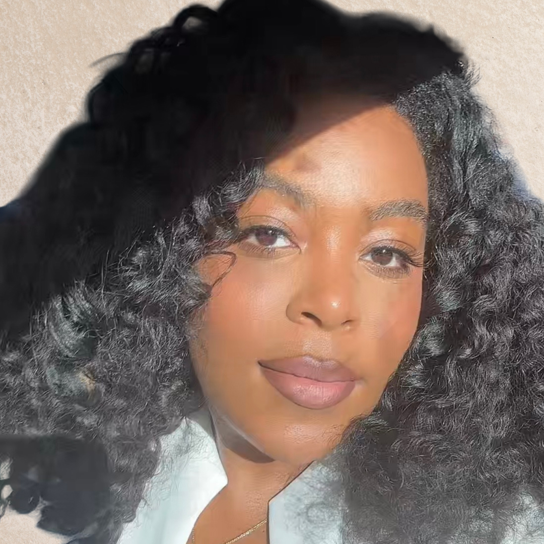 A woman with curly hair next to three tubes of lipstick in front of a light beige background. 