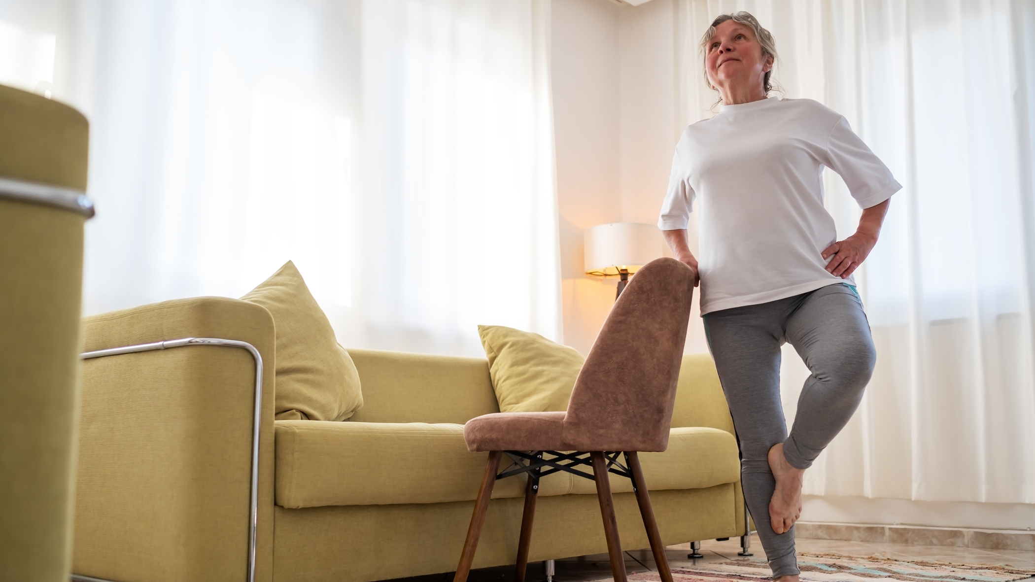 Woman stands on one leg, resting her hand on the back of a chair