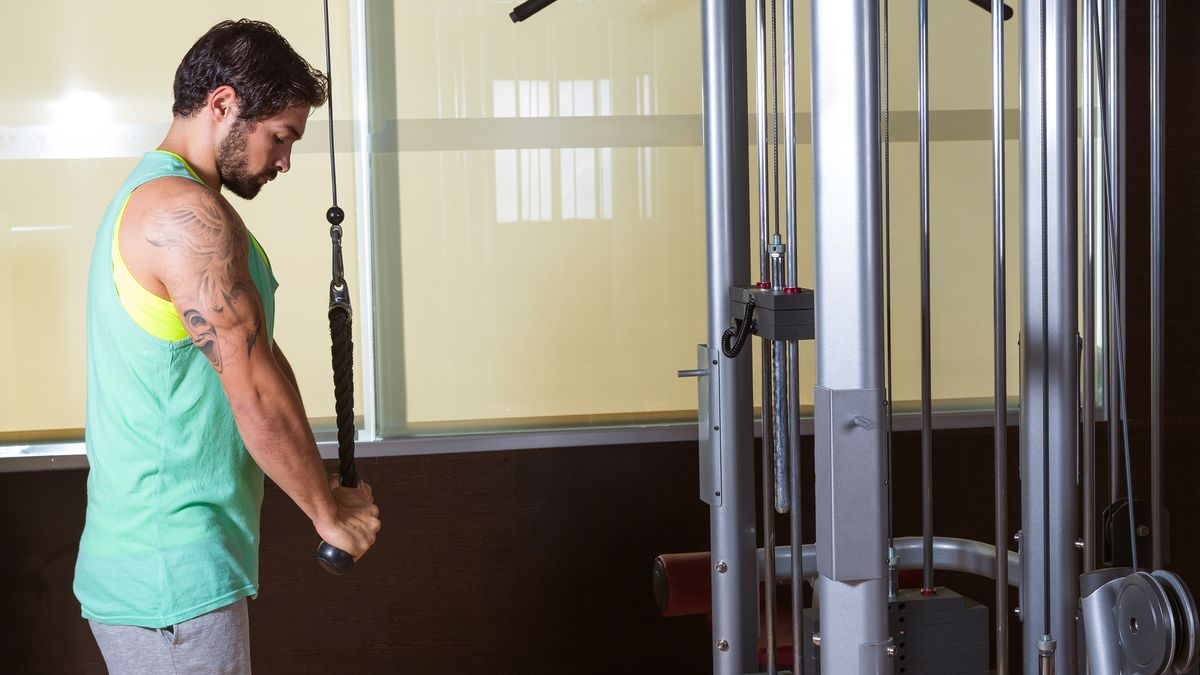 Man performing rope triceps press-down in gym on cable machine