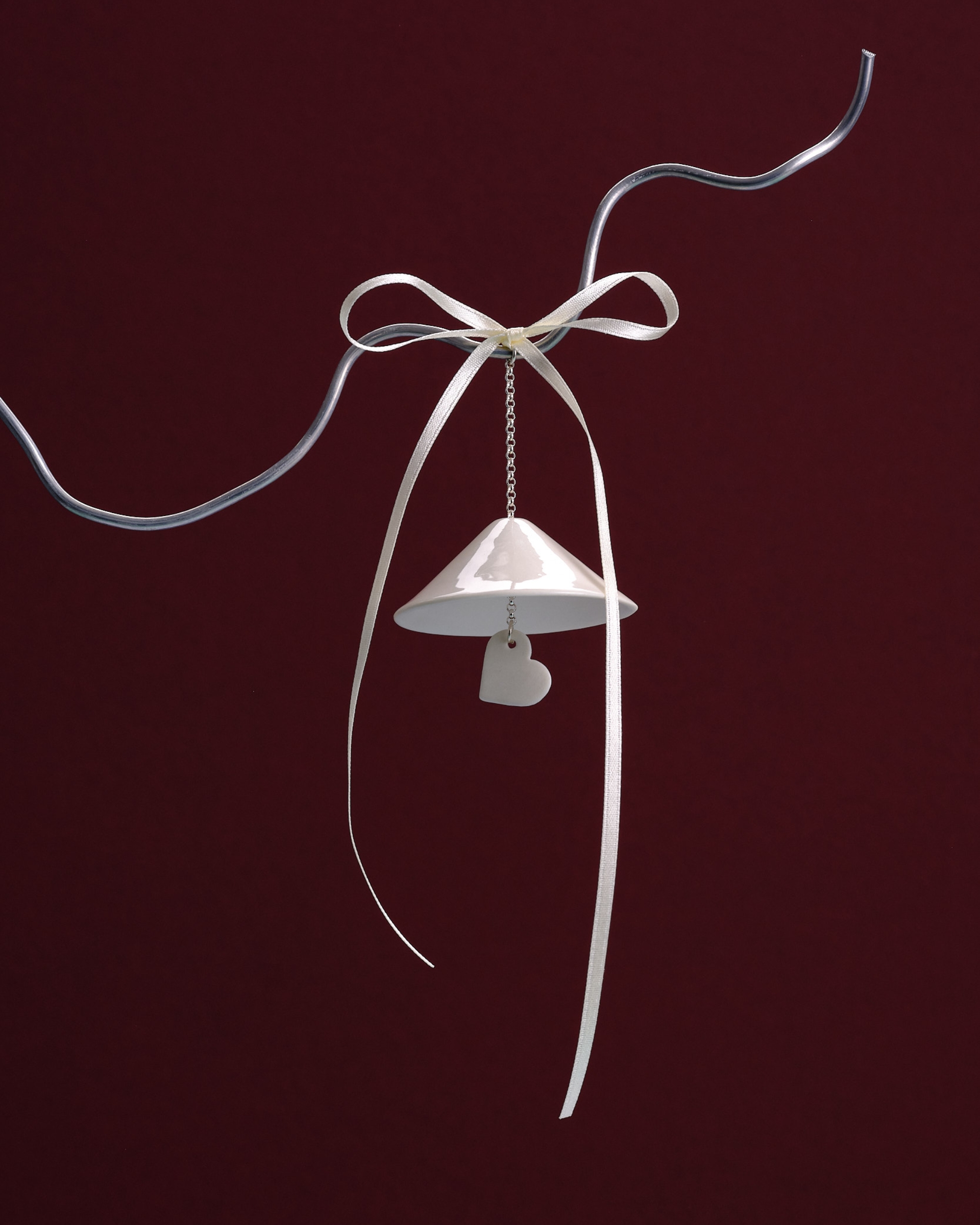 Image of two silver Christmas bell ornaments hanging on a silver wire in front of a burgundy background.