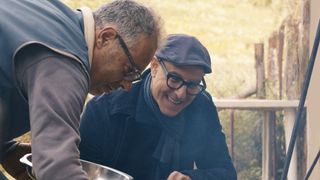 Stanley Tucci smiling as he kneels over a grill in Tucci in Italy