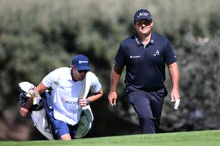 Patrick Reed walks along the fairway with his caddie behind him