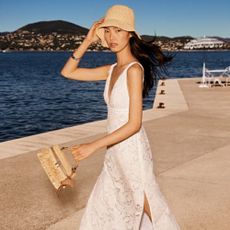 Young woman wearing Michael Kors dress, hat, and bag with sea in background