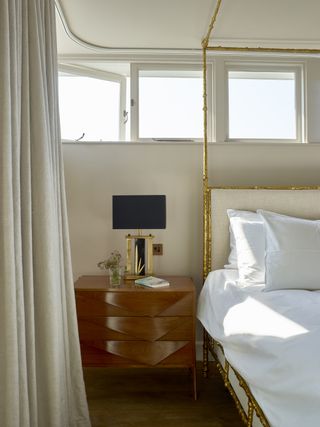 Bedroom with gold four poster bed, grey curtains and white bedding