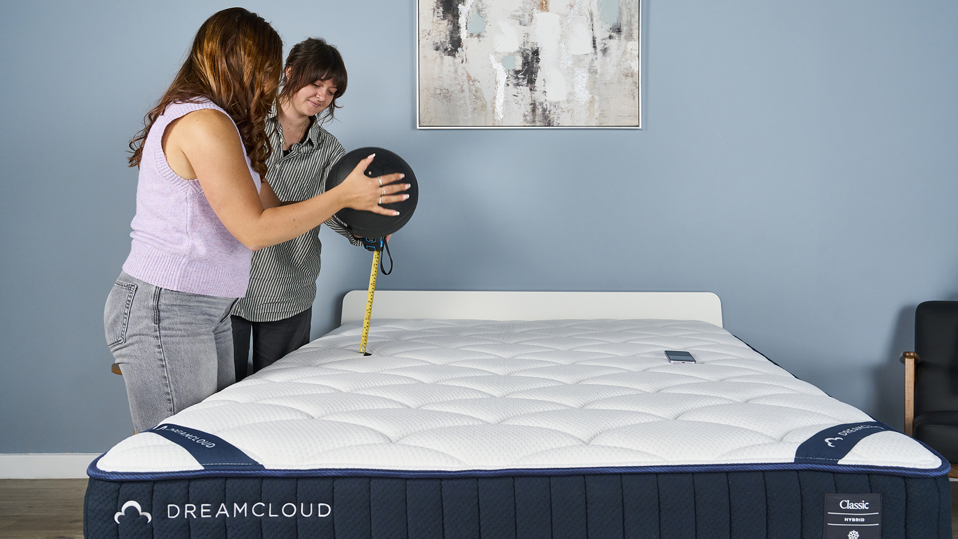 Two Tom's Guide testers setting up the motion isolation test. One is holding a 5kg slam ball above the mattress, while the other measures its height. An accelerometer is on the other side of the mattress