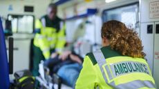 two medical providers in an ambulance wearing bright uniforms and preparing to slide a man on a stretcher out of the vehicle