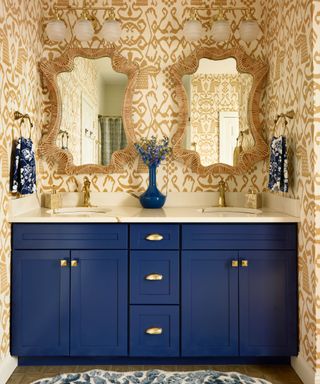 bathroom with double sink over dark blue dresser, neutral patterned wallpapered wall with double mirrors