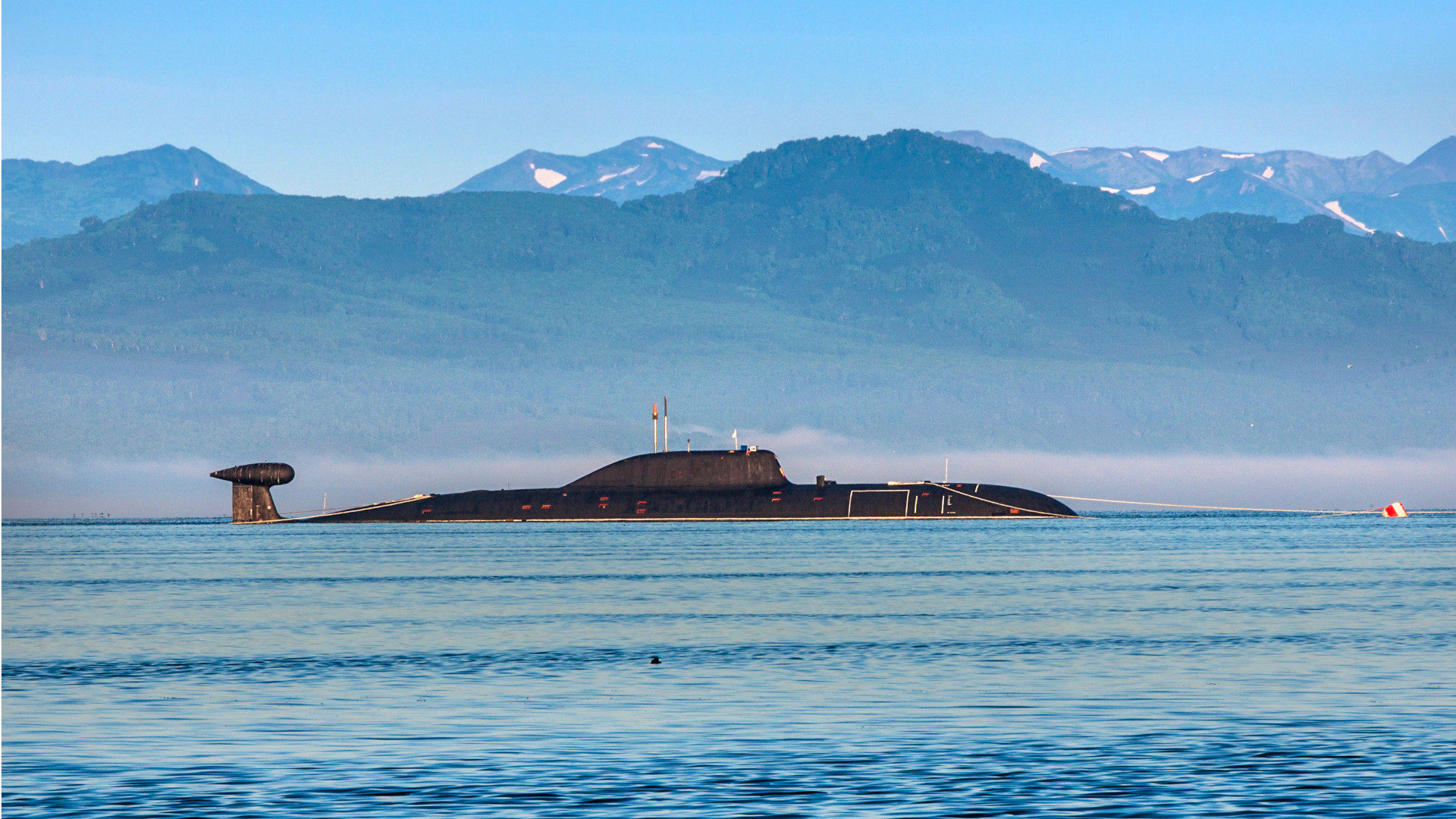 A Russian Akula-class submarine surfaced in the Pacific Ocean with mountainous terrain in the background.