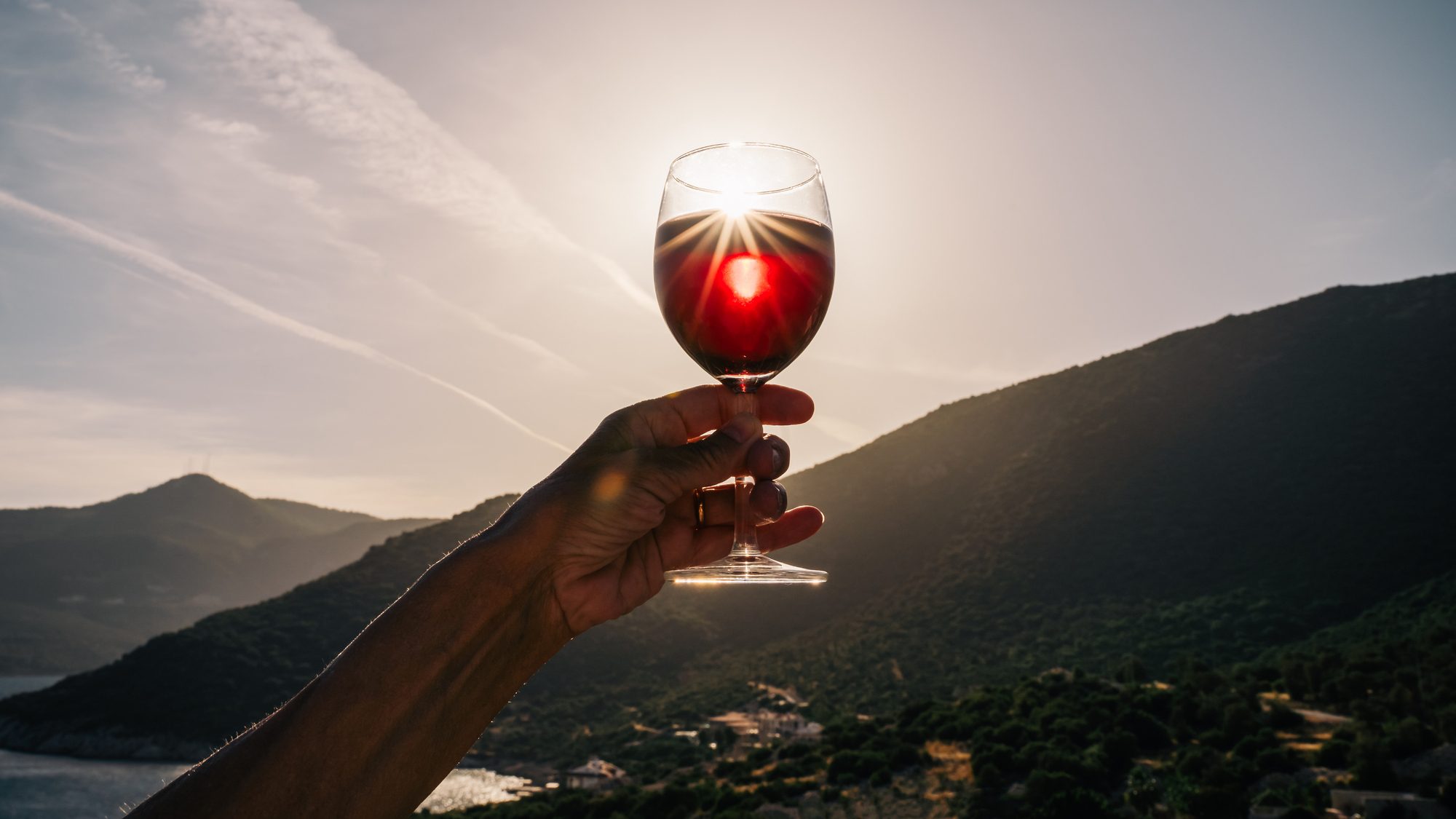 A glass of dark wine is held up to the sun causing a lens glare.
