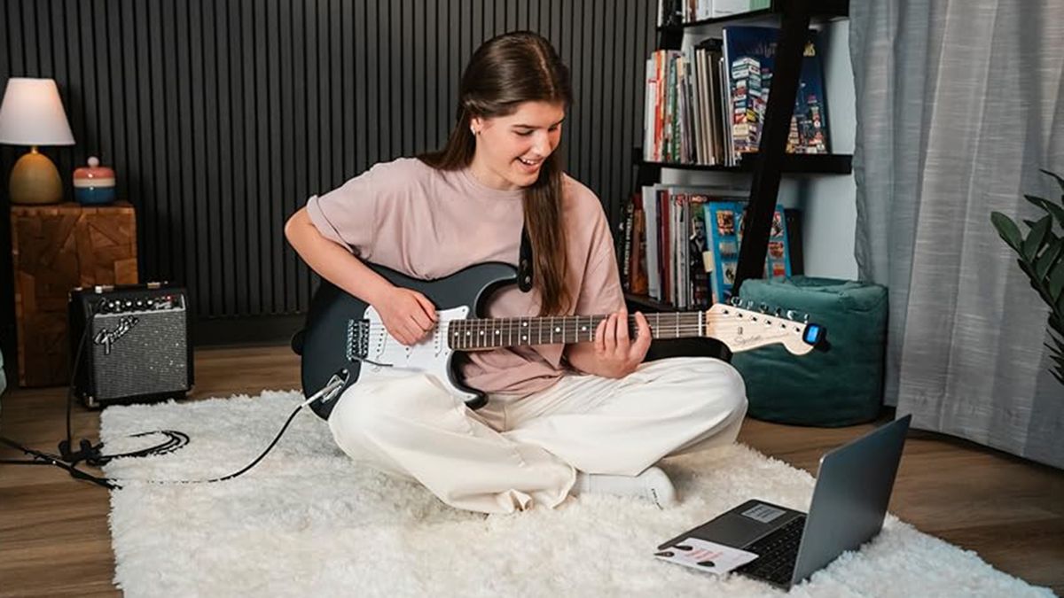 A girl playing a Squier Debut Stratocaster on the floor of her bedroom