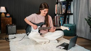 A girl playing a Squier Debut Stratocaster on the floor of her bedroom