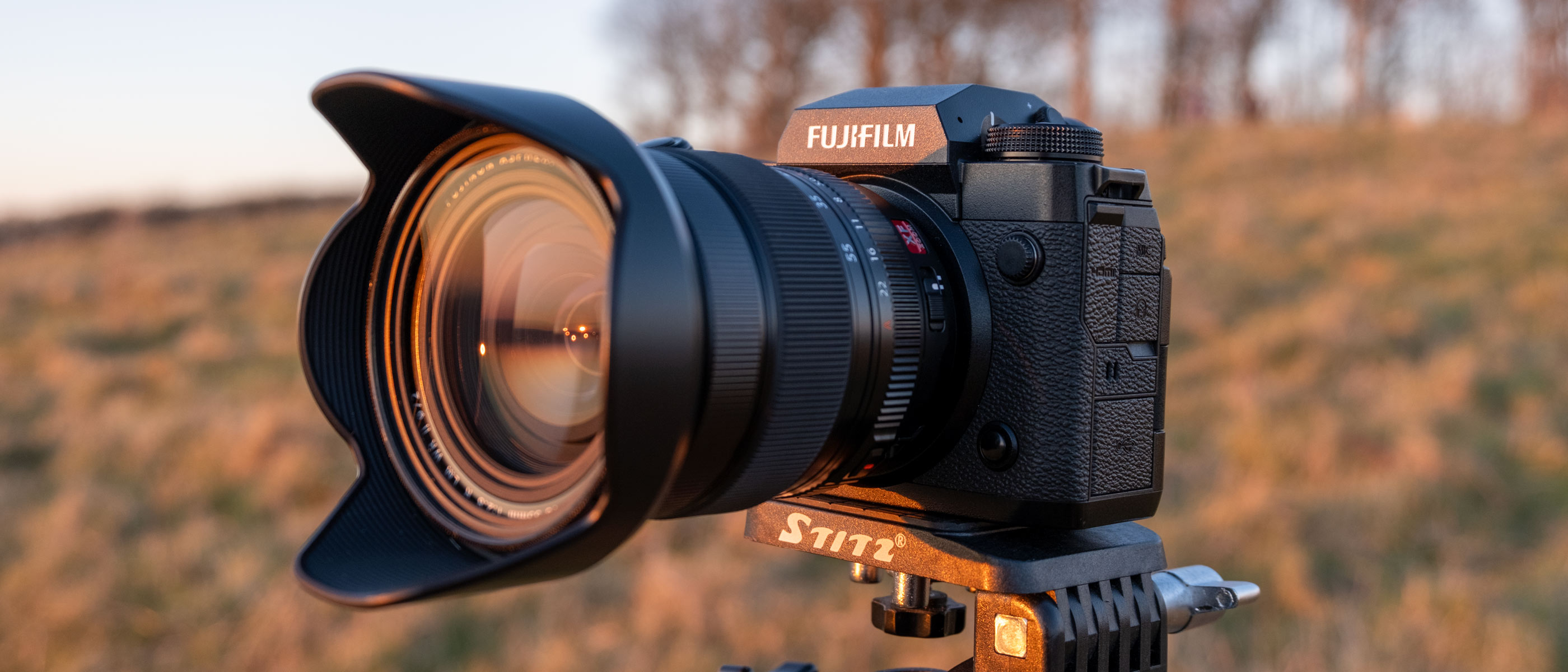 A Fujifilm X-H2 with zoom lens on a tripod in a field.