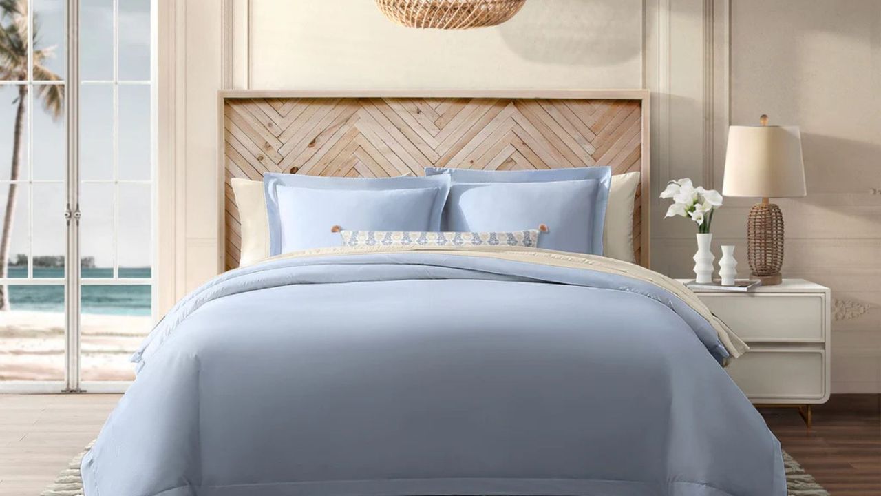 Light blue and cream sheets on a wooden bed frame on a cream wall; to the right, a white wooden nightstand.